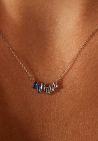 Zilveren ketting met een reeks afwisselende blauwe en heldere rechthoekige edelstenen, gezet in verlengde klauwen.
