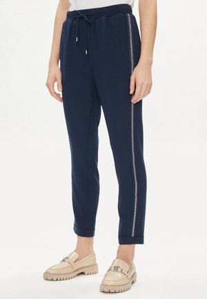 Pantaloni jogger blu navy con vita elasticizzata, tasche laterali, bordo in catena argentata lungo la cucitura esterna, gamba leggermente affusolata e caviglie con orlo. 