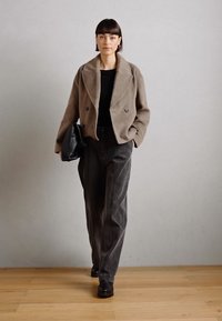 Beige ull dubbelknäppt kavaj över en svart topp, kombinerad med högmidjade grå byxor och svarta stövlar. Svart kuvertväska i handen.