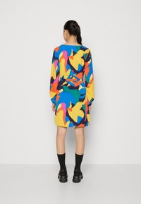 Robe à manches longues colorée présentant des motifs abstraits en jaune, bleu, rose et vert. Le matériau semble léger ; l'ourlet est au-dessus du genou.