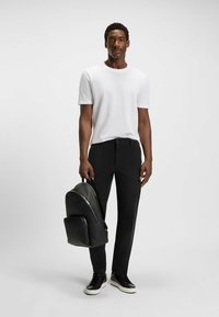 Biała, krótka koszulka z fakturowanym wzorem, zestawiona z czarnymi spodniami. Uzupełniona czarnym plecakiem o fakturowanej powierzchni i czarnymi trampkami.