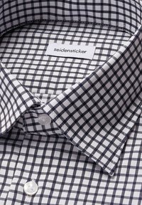 Close-up van een net gevouwen witte overhemd met een marineblauw geruit patroon, witte knopen en een zichtbaar "seidensticker" label aan de binnenkant van de kraag.