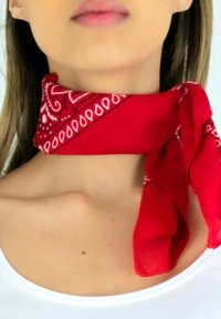 Écharpe de style bandana rouge nouée autour du cou, avec un motif paisley blanc et des accents diagonaux. Tissu léger avec une texture lisse.