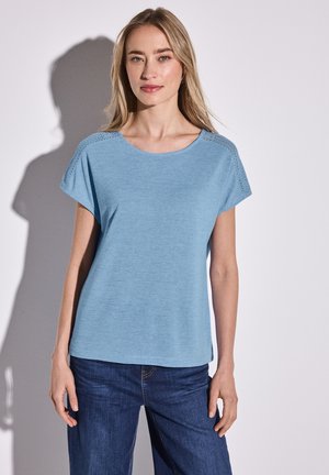 Haut bleu clair à manches courtes avec un col rond. Présente des détails texturés sur les épaules. Tissu lisse coupé avec une coupe décontractée.