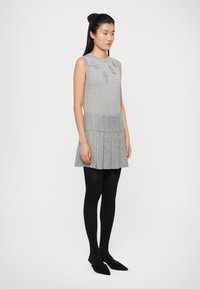 Vestito grigio lavorato a maglia con corsetto aderente e gonna plissè. Presenta applicazioni floreali sul petto. Indossato con calze nere e ballerine a punta.