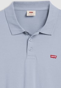 Light blue polo shirt made of cotton, with a ribbed collar, two-button placket, and a red Levi's logo on the left chest.