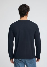 Navyblå långärmad t-shirt med rund halsringning och avslappnad passform, tillverkad av mjukt bomullstyg, visad bakifrån.