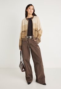 Καδαρίνι σε μπεζ και καφέ ρίγες, μαύρο τοπ, φαρδιά καφέ παντελόνια και μαύρη τσάντα, με διακοσμητική ζώνη με τρουκ.