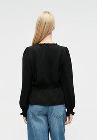 Musta pusero, jossa on teksturoitu pinta, pussihihat ja aaltoileva pääntie. Yhdistetty vaaleansinisiin leveälahkeisiin farkkuihin.