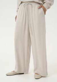 Pantalons larges beige clair en tissu léger, dotés d'une taille élastique avec cordon de serrage, de poches latérales et d'une finition lisse et texturée.