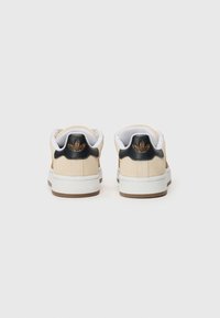 Beige semskinn sneakers med svarte hæl aksenter, polstret krage, hvite snørebånd og en teksturert gummisåle. Dekorativ logo på hælen.
