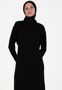 Black long-sleeve dress with a ribbed texture, high collar, and relaxed fit, complemented by a matching black headscarf.