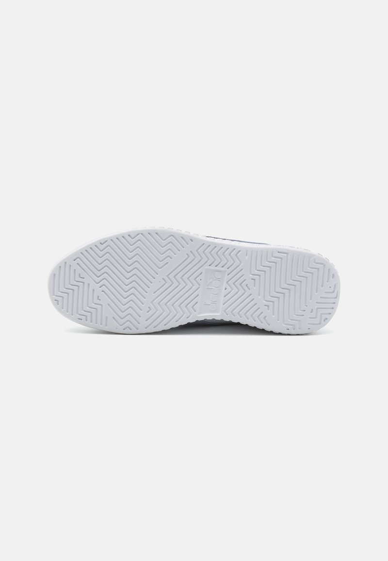 Suola di una sneaker in gomma bianca, con un motivo a spina di pesce e un logo rettangolare al centro.