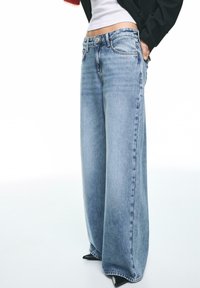 Jeans a gamba larga di colore azzurro chiaro in denim. Caratterizzati da una vita alta, tasche frontali standard e una leggera texture sbiadita. Abbinati a scarpe nere a punta.