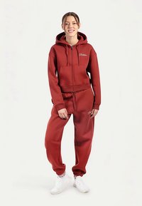 Czerwona bluza z kapturem na pełny zamek, z kieszeniami typu kangurka i haftowanym logo, w zestawie z dopasowanymi spodniami dresowymi. Gładka, miękka tkanina.