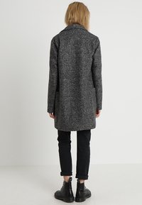 Grijze wollen jas met een gestructureerde afwerking, lange mouwen, een reverskraag en zijzakken, gecombineerd met zwarte opgerolde broekspijpen en laarzen.