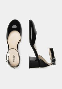 Décolleté nere in pelle verniciata con cinturino alla caviglia, tacco quadrato chunky e punta arrotondata liscia. Fodera interna beige con marchio. Dettaglio con fibbia regolabile.