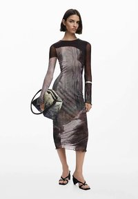 Strak zittende jurk met een mix van donkere en lichte abstracte patronen, lange mouwen en een ontwerp tot op de knie. Gecombineerd met een klein tasje.