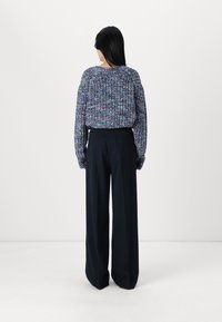 Texturert, flerfargede strikkede gensere med bred hals, kombinert med løstsittende, høyt liv svarte bukser.