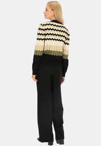 Sweter dzianinowy w wzór zygzak w kolorze kremowym, czarnym i oliwkowym, z prążkowanym wykończeniem i długimi rękawami. Czarne spodnie o szerokich nogawkach.