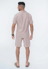 Chemise beige à manches courtes et col, assortie à un short. Fabriquée en tissu lisse, avec une coupe décontractée et un design simple. Chaussures décontractées.