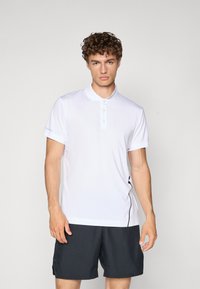 Fehér póló ing gombos nyakkal és rövid ujjakkal, fekete sorttal párosítva. Oldalsó díszítés jellemzi cipzár részlettel.