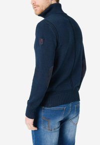 Marineblauer Strickpullover mit hohem Kragen, gerippten Bündchen und Ellenbogenpatches. Verfügt über ein strukturiertes Gewebe und ein kleines Logo auf der Schulter.