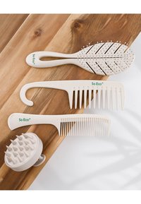 Fire hårpleieverktøy: en bladformet børste, to kammer - en med krok - og en hodebunnsmassør, alle i kremfarget, teksturert plast.