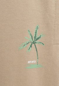 Beige szövet textúrált felülettel, zöld pálmafa grafikával és alatta fehér betűkkel a "JUST RISE" felirattal.