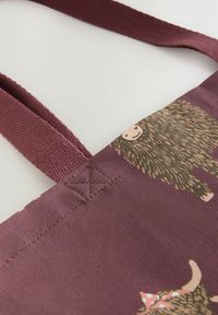 Reusable tote bag in burgundy fabric featuring animal patterns, sturdy woven straps, and reinforced stitching at strap attachment points.