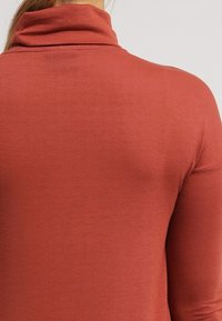 Rostfärgad polotröja, ribbad textur, figurnära design, långa ärmar, slät tyg utan synlig hårdvara eller mönster.