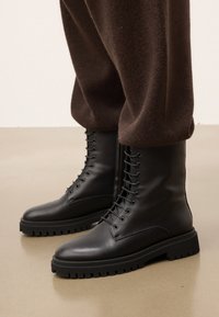 Stivali da combattimento neri in pelle con punta rotonda, design di allacciatura sicura e suola in gomma robusta, con superficie texturizzata e battistrada spesso.