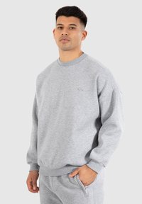 Sweatshirt gris en tissu mélange coton avec col rond, poignets et ourlet côtelés. Présente un logo discret sur la poitrine. Coupe simple et décontractée.