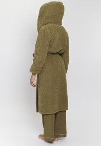 Olivgrön huva klädnad gjord av fluffig, strukturerad tyg med knytning vid midjan. Den är kombinerad med matchande vida byxor med en ljus kant.