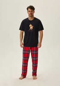 Koszulka z krótkim rękawem w kolorze granatowym z grafiką psa, zestawiona z czerwonymi spodniami dresowymi w kratę z czarnymi i niebieskimi akcentami. Miękka tkanina, luźny krój.