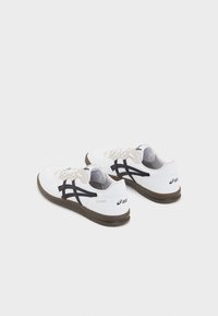 Adidași albi cu accente negre, superior din piele, zona vârfului perforată și o talpă din cauciuc maro. Au șireturi și un logo pe toc.