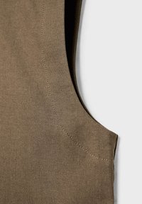 Tissu en lin marron avec détail de couture visible et une découpe pour l'emmanchure sur fond blanc.