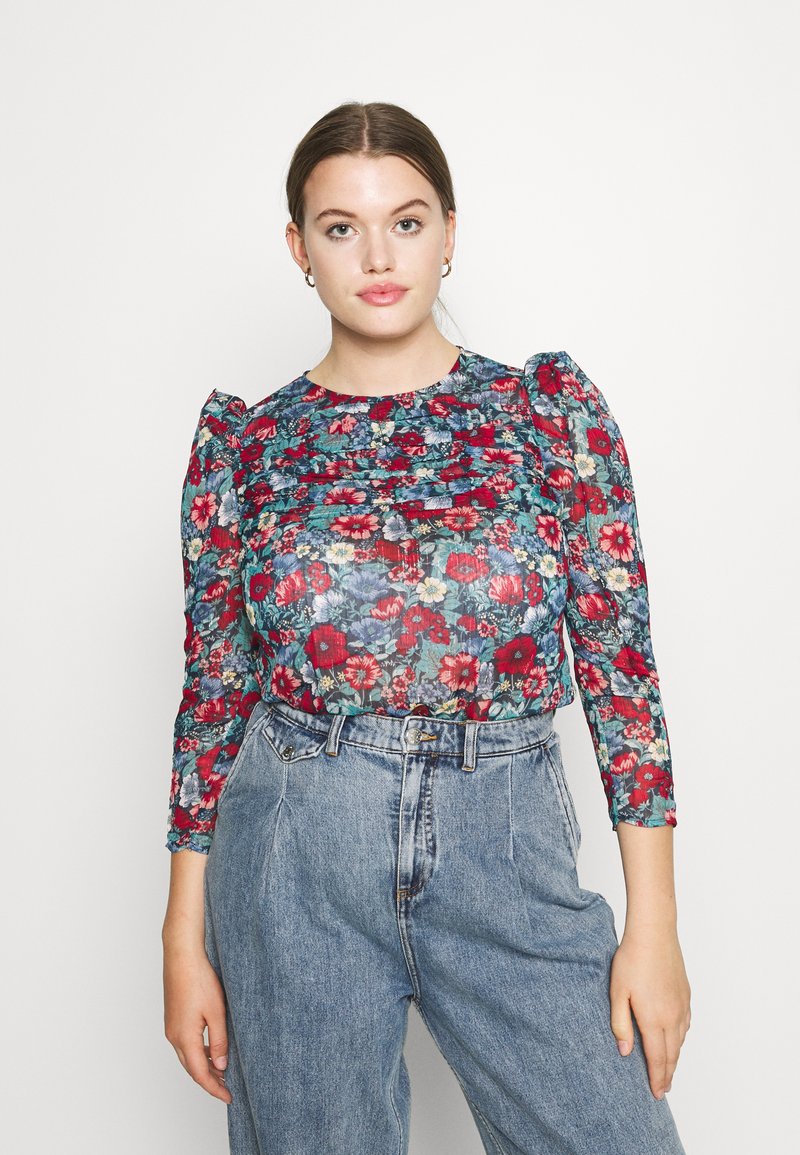 Blusa floreale in tessuto trasparente con vivaci fiori rossi e blu. Maniche lunghe con leggero effetto a sbuffo e design frontale arricciato.