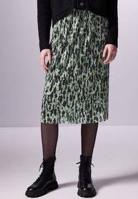 Zelená a černá plisovaná midi sukně s texturovaným vzorem, doplněná černými bojovými botami a černými poloprůhlednými punčochami.