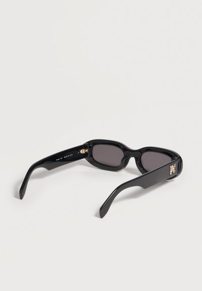 Lunettes de soleil rectangulaires noires avec verres foncés et initiales décoratives dorées sur les branches épaisses, présentées sur un fond neutre.