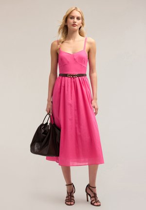 Roze midi-jurk met spaghettitjes, aansluitende bodice, gerimpelde taille en een bruine riem. Gepaard met een zwarte handtas en gestrikte hakken.