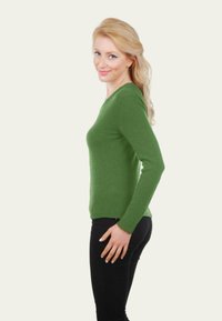Un pull vert à manches longues avec un col rond, de coupe ajustée et une texture douce. Porté avec un pantalon noir, mettant en avant un profil latéral.