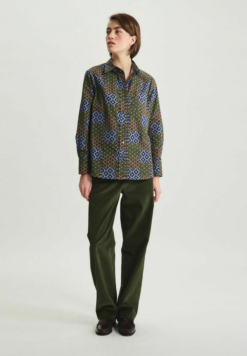Chemise à motif floral dans des tons vert, bleu et marron ; associée à un pantalon en velours côtelé vert foncé et des chaussures marron.