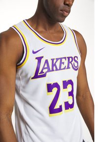 Bijela košarkaška dres ima natpis "Lakers" u žutoj i ljubičastoj boji, broj "23" u žutoj boji obrubljenoj ljubičastom, sa mrežastom teksturom i dizajnom na ramenima.