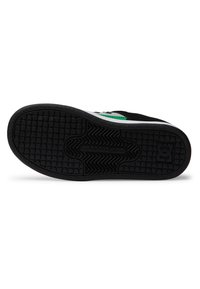 Sola de sneaker preta com padrão de aderência texturizado e ligeiras indentação circulares. Detalhes brancos com detalhes verdes perto do calcanhar.