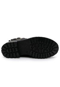Zwarte schoenen met een extreem rubberen zool met een profiel, accenten van metalen hardware en een meerlagige constructie voor duurzaamheid.