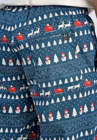 Katoenen shorts met een blauwe achtergrond met witte sneeuwvlokken, rode sleeën, rendieren en sneeuwmannen. Inclusief een geïntegreerde zak en label.