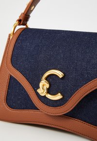 Brun læderpung og marineblå denimtaske med bølget design, guldfarvet hardware og et fremtrædende sammenfiltret "C" logo.