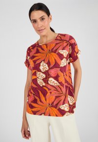 Blusa a manica corta color bordeaux con stampa floreale. Presenta foglie di un vivace arancione, rosa e crema. Texture morbida e vestibilità comoda.