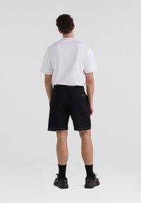 Svarta shorts med vit sömnad, fickor och en avslappnad passform, tillsammans med en vit kortärmad skjorta. Skorna är svarta sneakers.